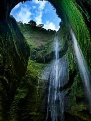 Stunning vertical waterfall inside a lush green cave under blue skies.
